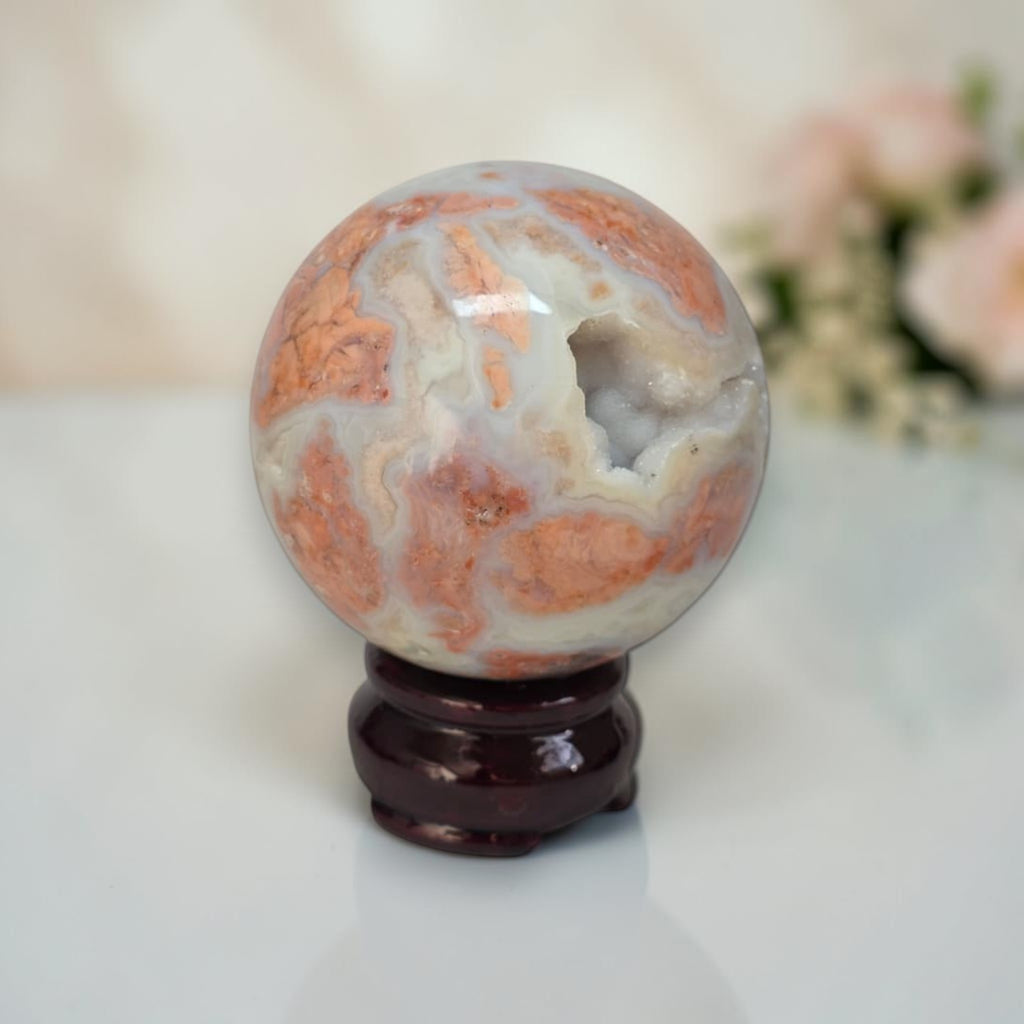 Marbled agate sphere with white, gray, and orange swirls on dark glossy stand