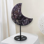 Purple speckled crescent moon crystal decor on black metal stand on white shelf