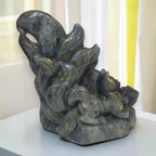 A carved stone sculpture of a fox nestled among leaves, displayed on a white surface with a softly lit indoor background.