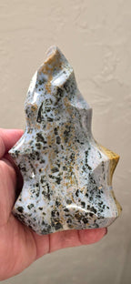 Freeform ocean jasper crystal flame held in hand, white-and-blue with black speckles