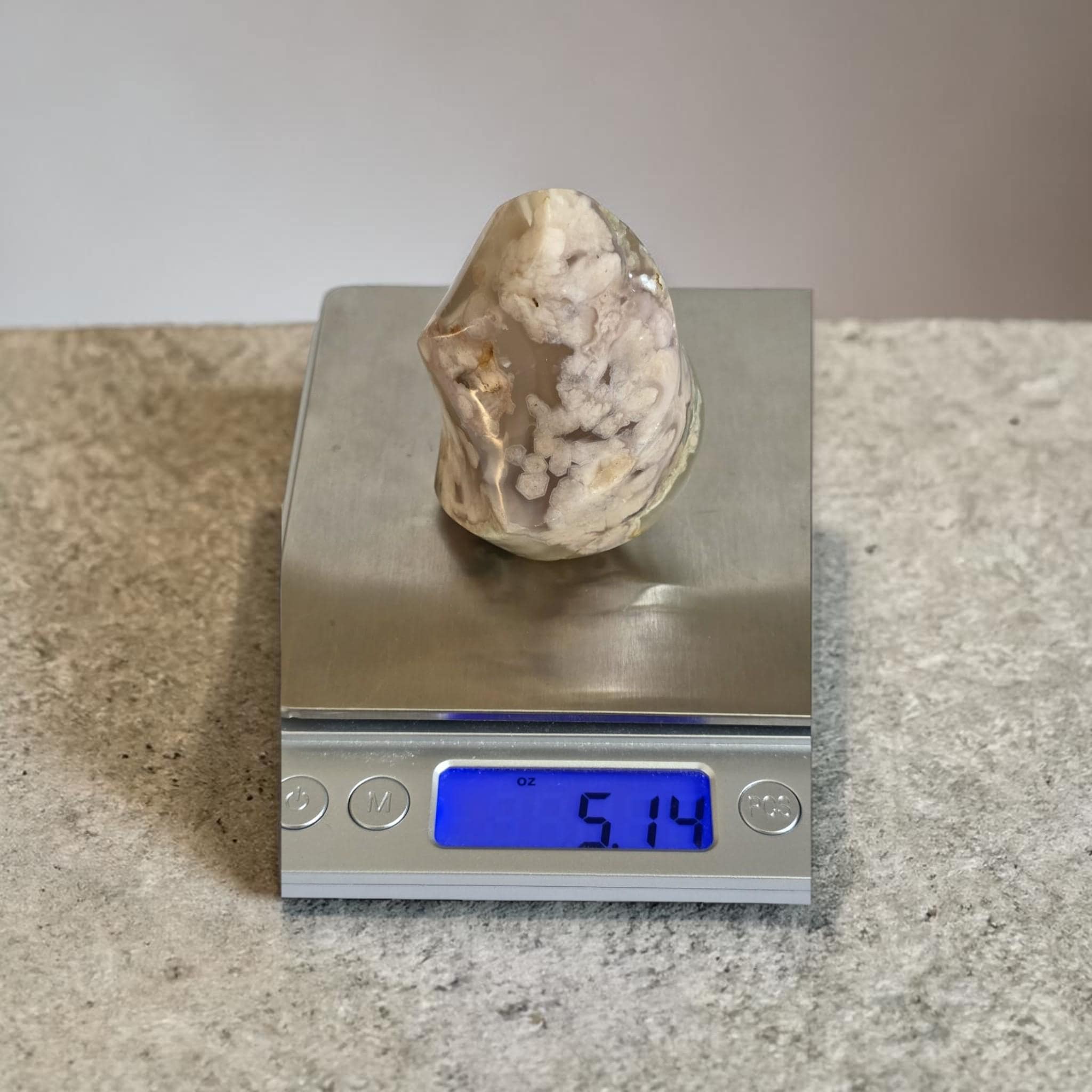 Agate flame crystal on a digital scale, clear beige with white mineral inclusions