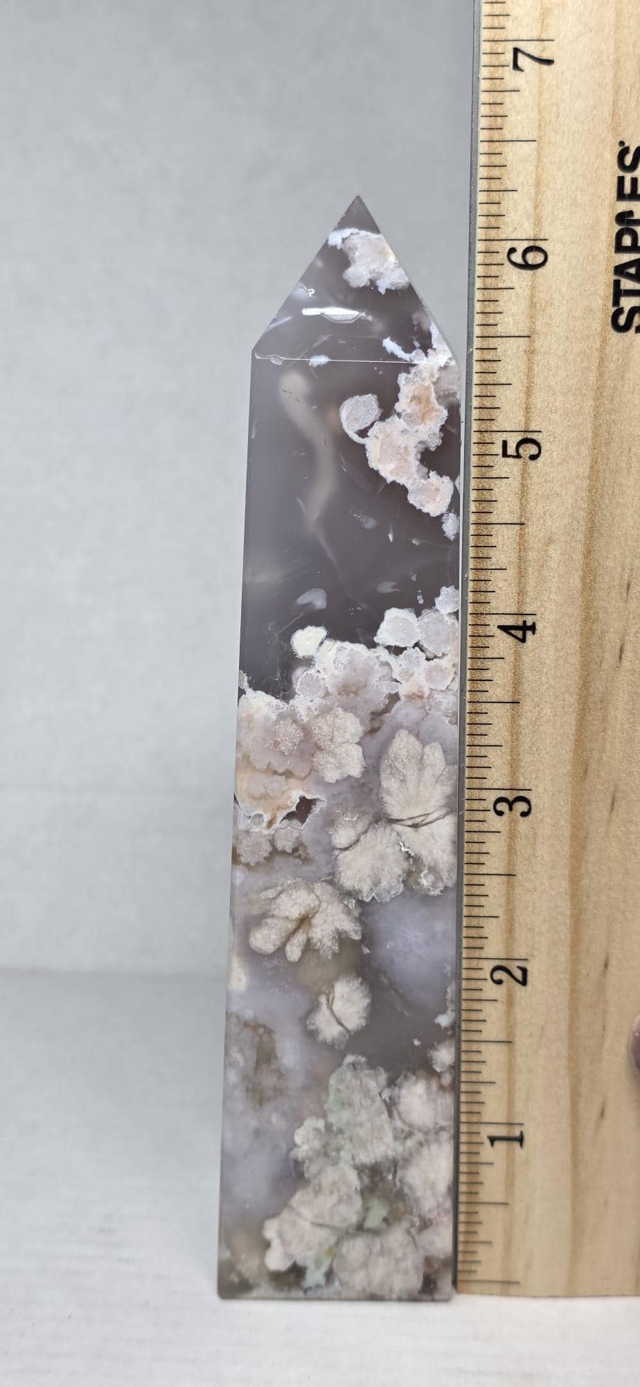 Flower agate crystal tower next to wooden ruler, dark gray with white inclusions