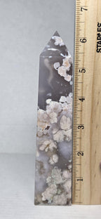 Flower agate crystal tower next to wooden ruler, dark gray with white inclusions