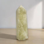 Pale yellow-green translucent crystal obelisk standing upright on tabletop, pointed top