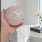 Rose quartz sphere held in hand, polished pale pink crystal