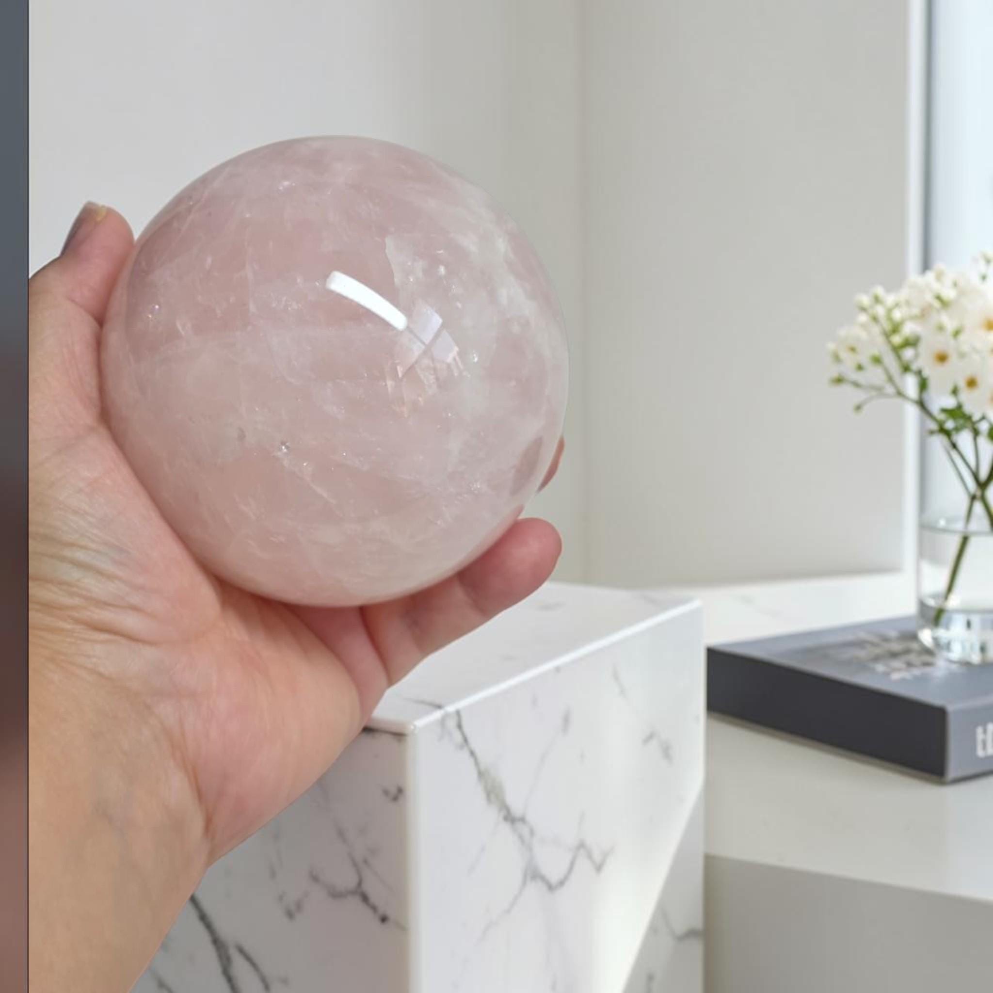 Rose quartz sphere held in hand, polished pale pink crystal