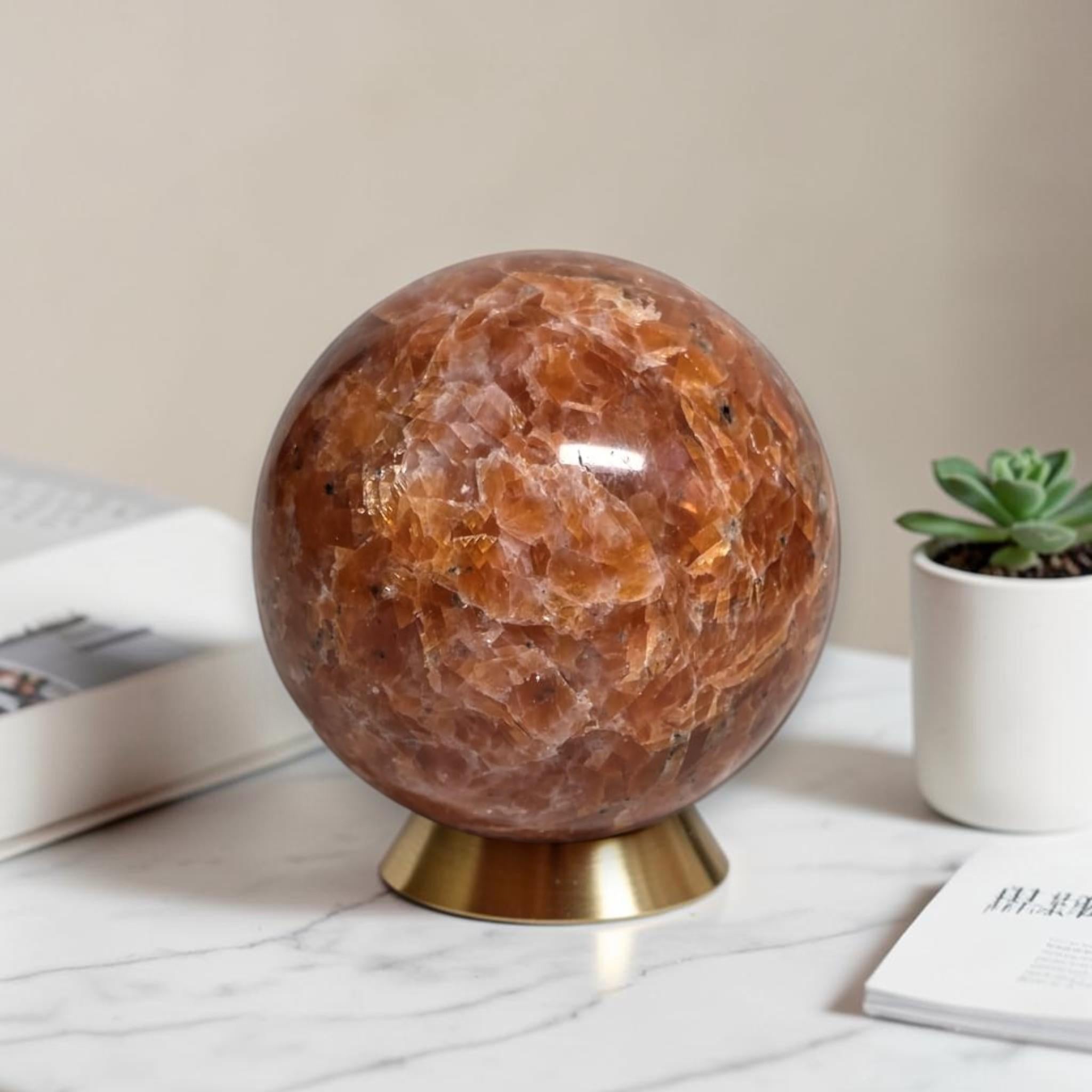 Orange sunstone gemstone ball, polished surface, on gold base stand