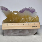 Eagle crystal carving with yellow wings and purple tips on gray base beside ruler