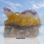 Back view of eagle crystal carving with yellow body, purple-tinted wings, gray base