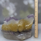 Eagle crystal carving with yellow body and purple wings on gray base next to measuring ruler