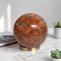 Polished natural orange sunstone sphere on gold display stand