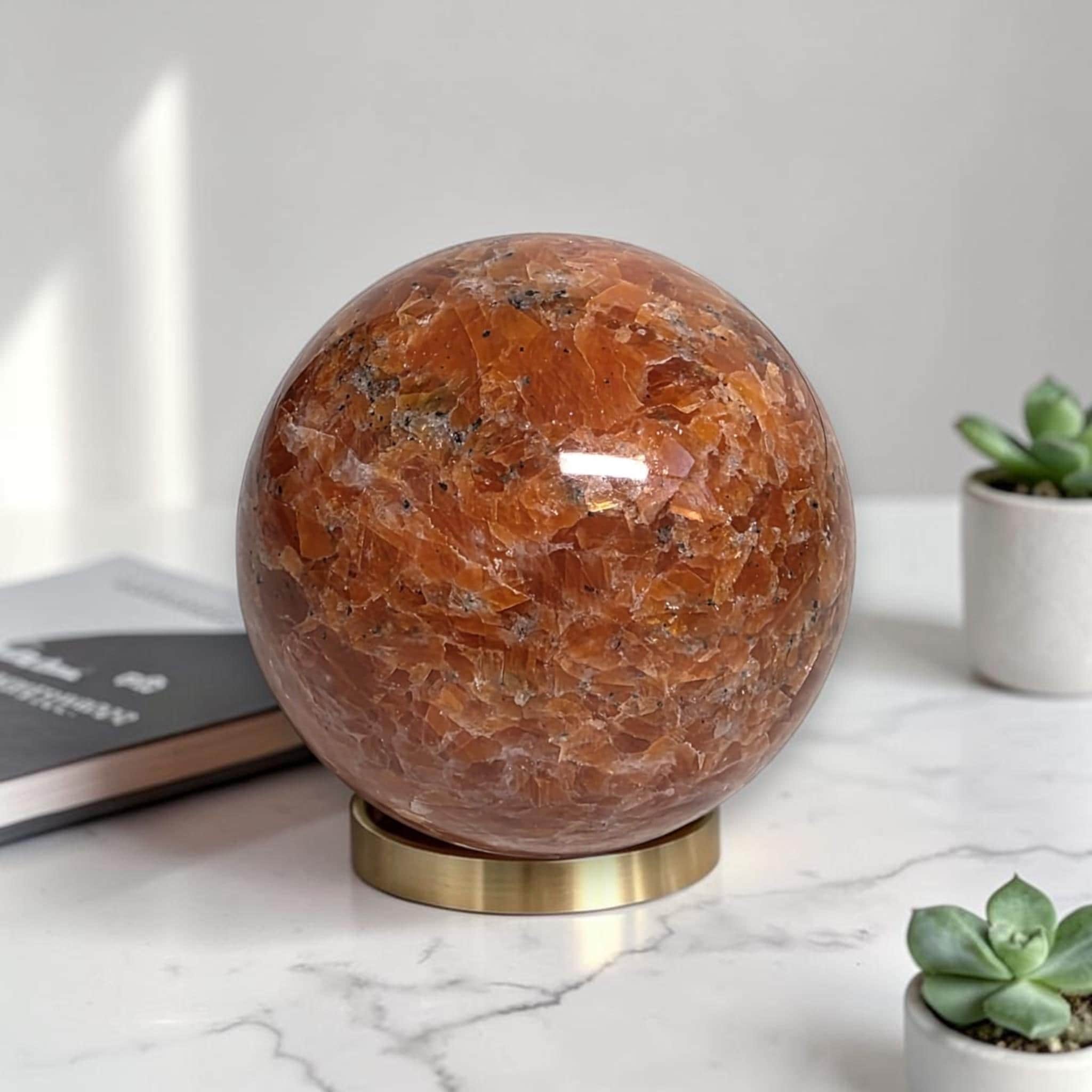 Polished natural orange sunstone sphere on gold display stand