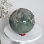 Green crystal sphere with mottled druzy pockets and white quartz clusters on red base