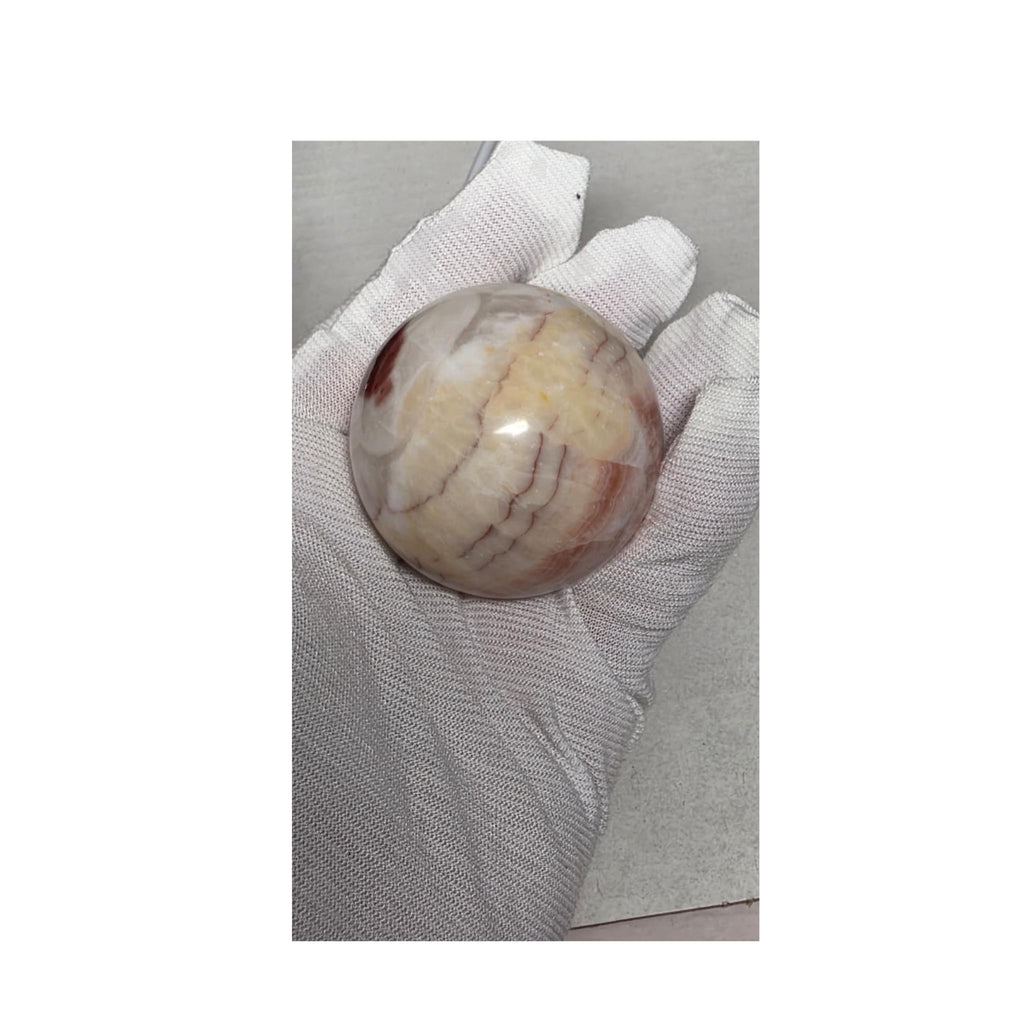 Pale calcite sphere with soft pink veining on wooden stand, held in white gloves.