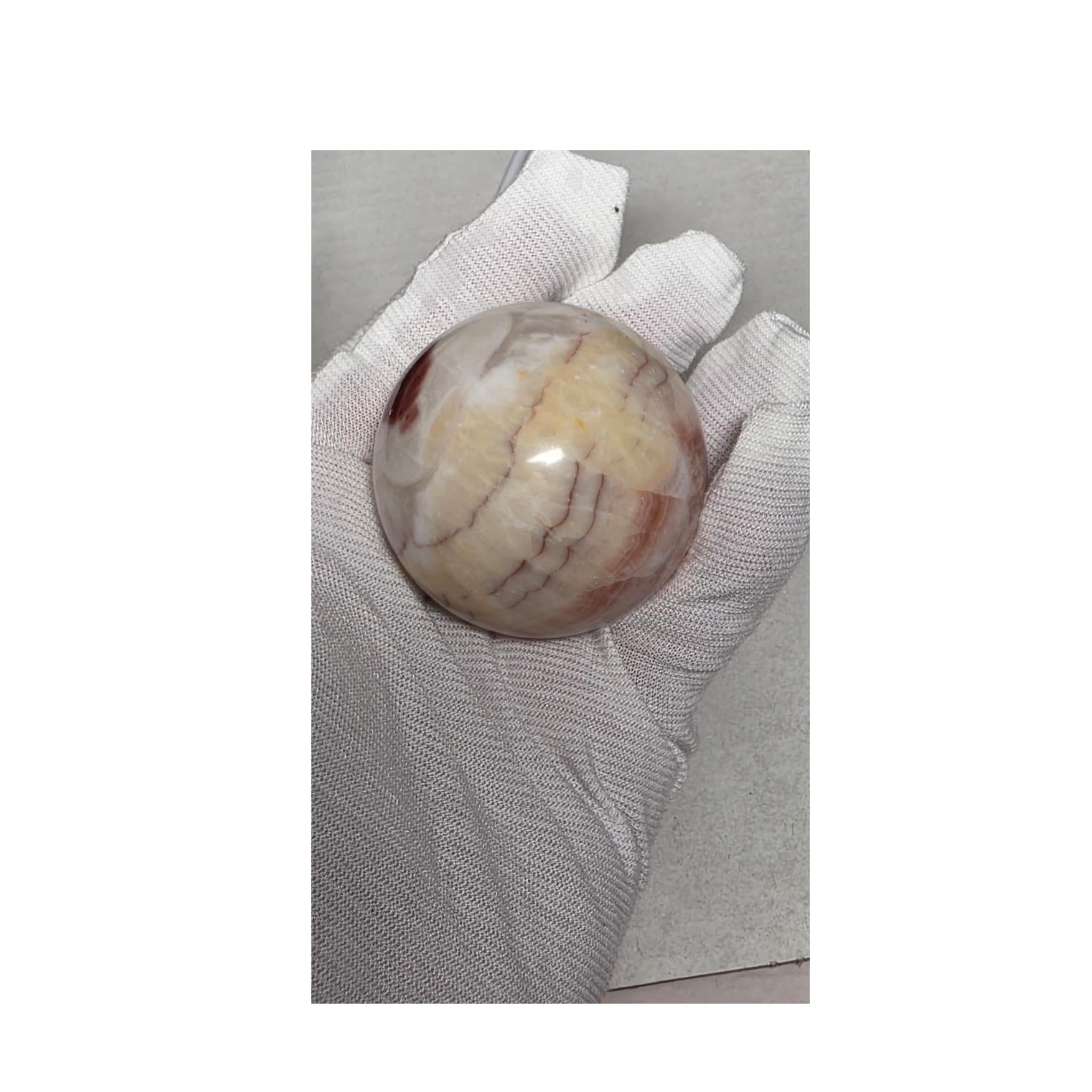 Pale calcite sphere with soft pink veining on wooden stand, held in white gloves.