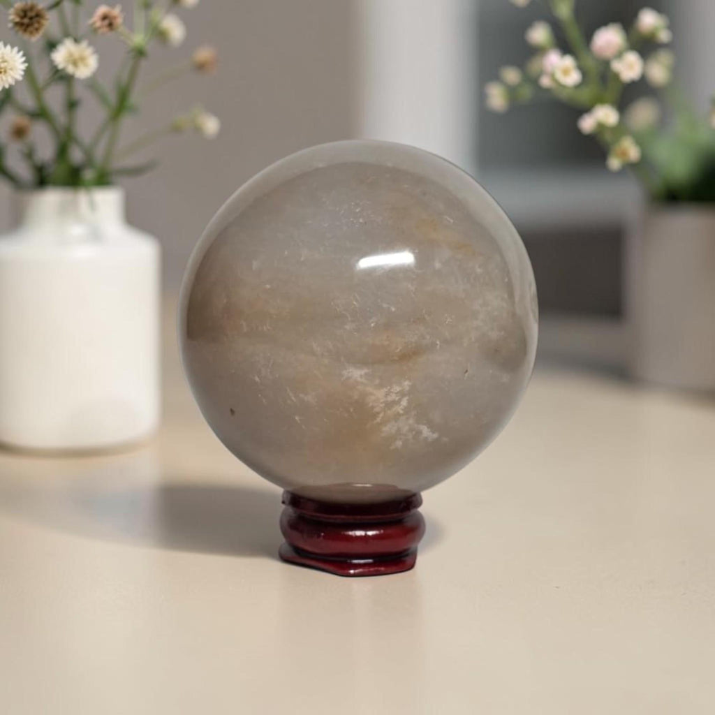 Honey calcite crystal sphere on dark red stand, translucent beige with light inclusions