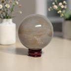 Honey calcite crystal sphere on dark red stand, translucent beige with light inclusions