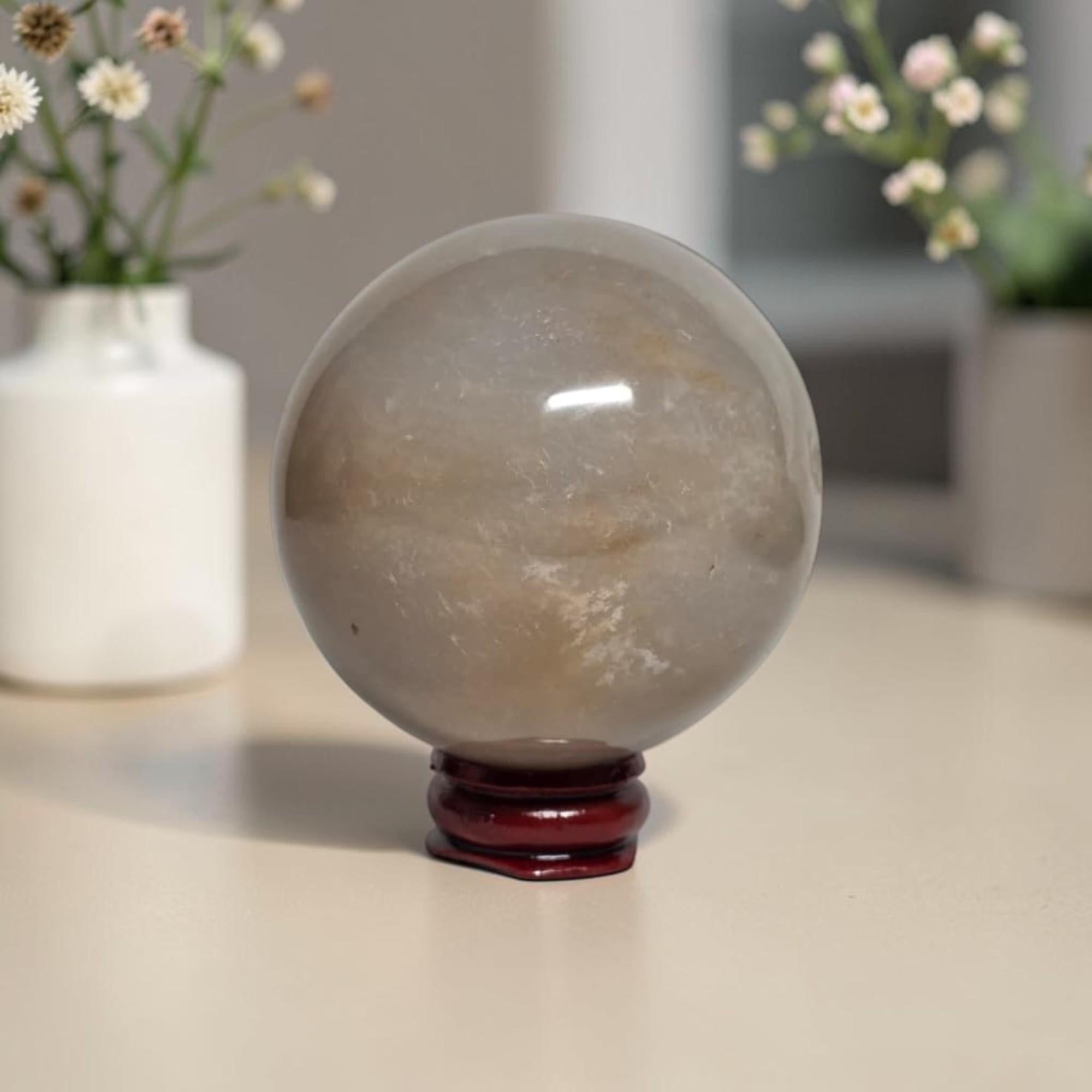 Honey calcite crystal sphere on dark red stand, translucent beige with light inclusions