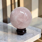 Rose quartz crystal ball on dark pedestal, smooth polished pale pink