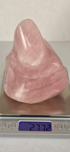 Rose quartz flame-shaped crystal on a scale, pink translucent with glossy polished face