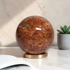Natural orange sunstone sphere with glossy finish on gold display base