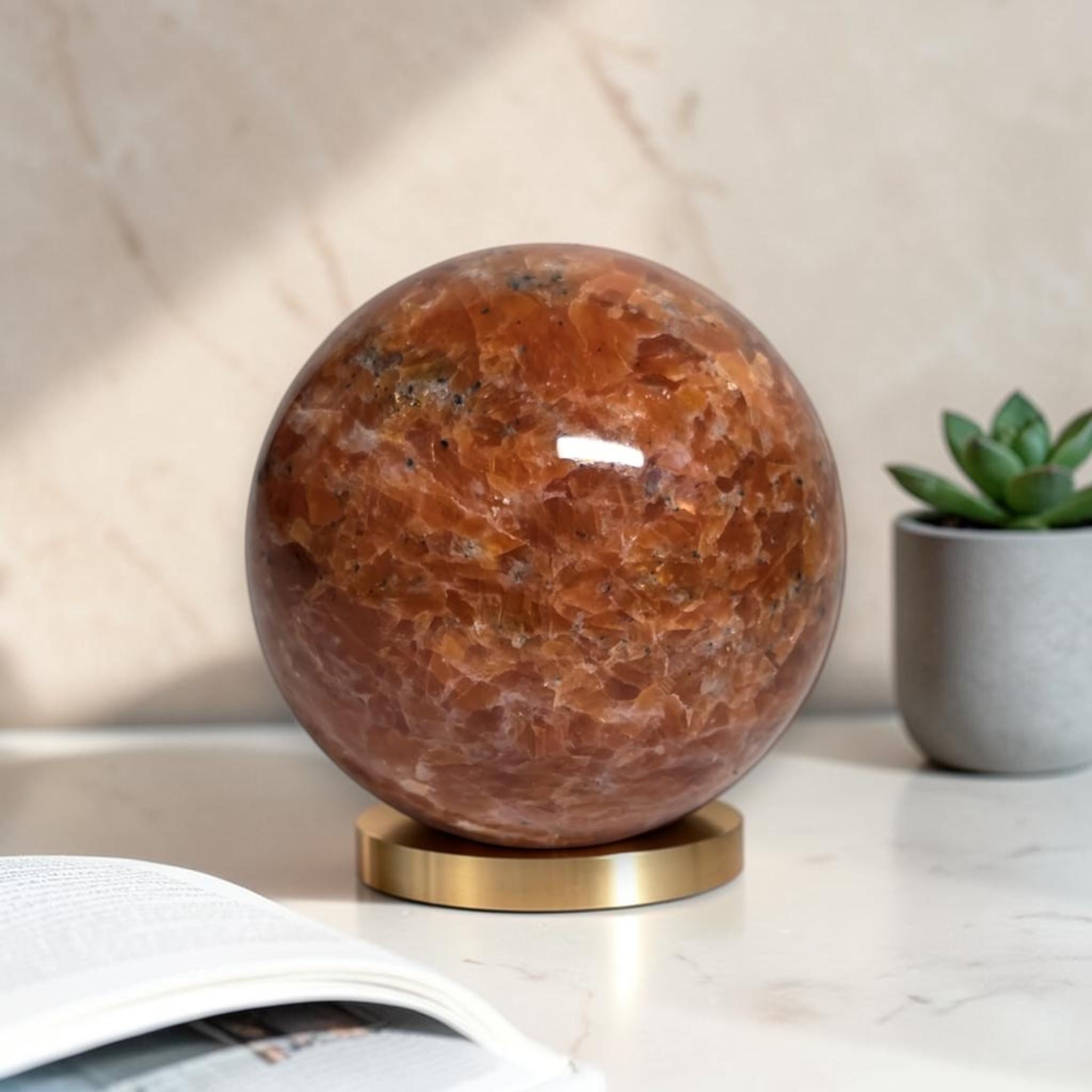 Natural orange sunstone sphere with glossy finish on gold display base