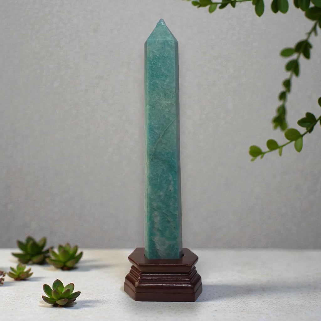 Green crystal obelisk with pointed tip on dark wooden stand