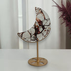 Fire quartz crescent moon with reddish brown and dark veining on a gold tone display stand