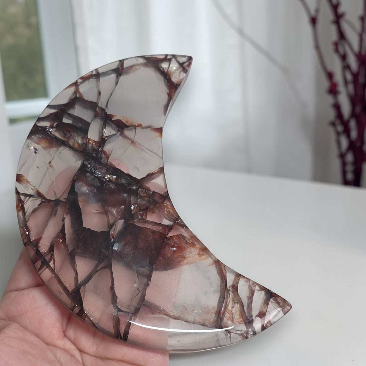 Fire quartz crescent moon held in a hand showing translucent areas and dark veining
