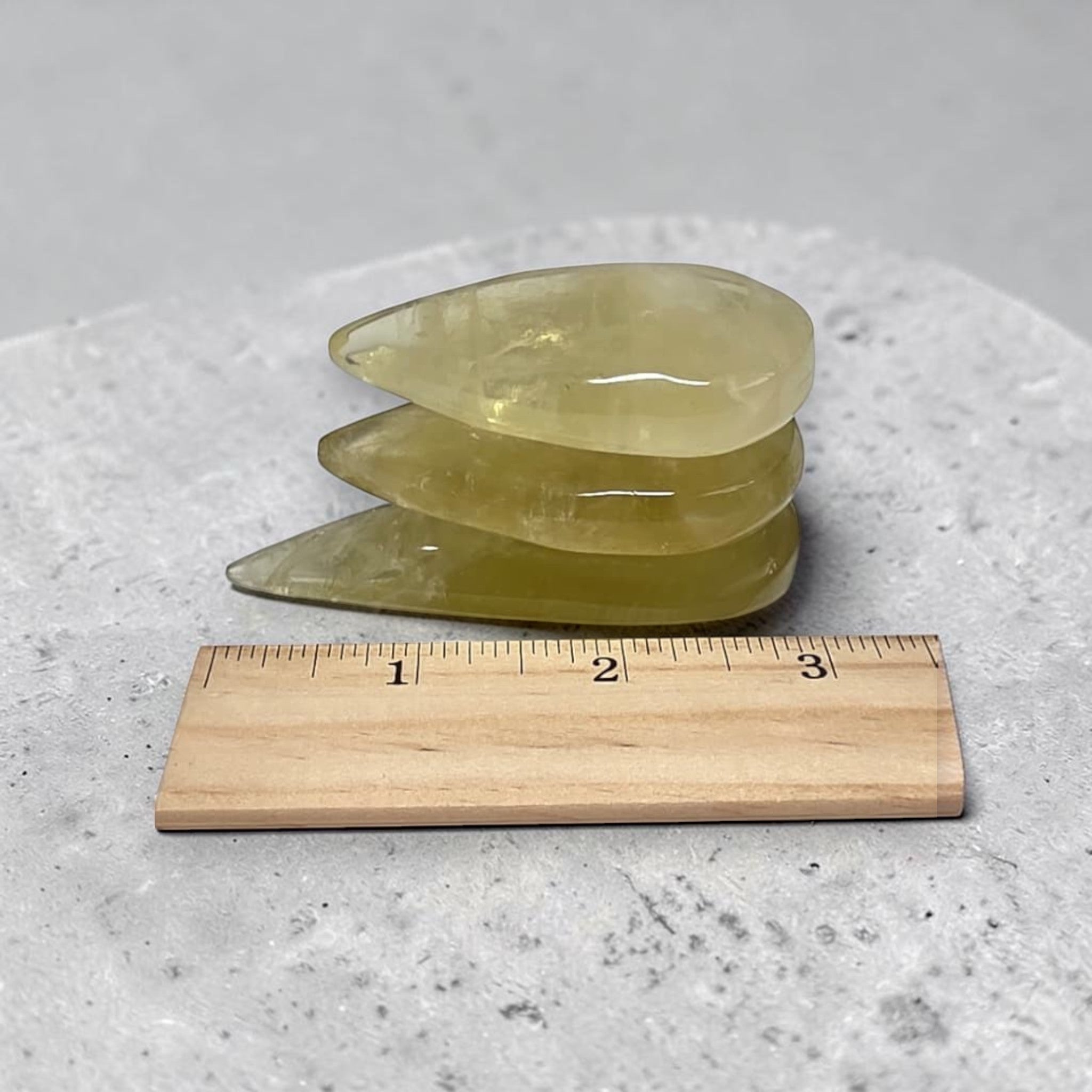 Three yellow crystal slabs with smooth, translucent surfaces beside a 1–3 in ruler