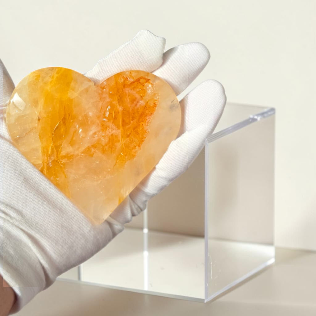 Heart-shaped orange stone held by a gloved hand on a white background