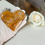 Heart-shaped amber stone on a white cloth with a white rose beside it.
