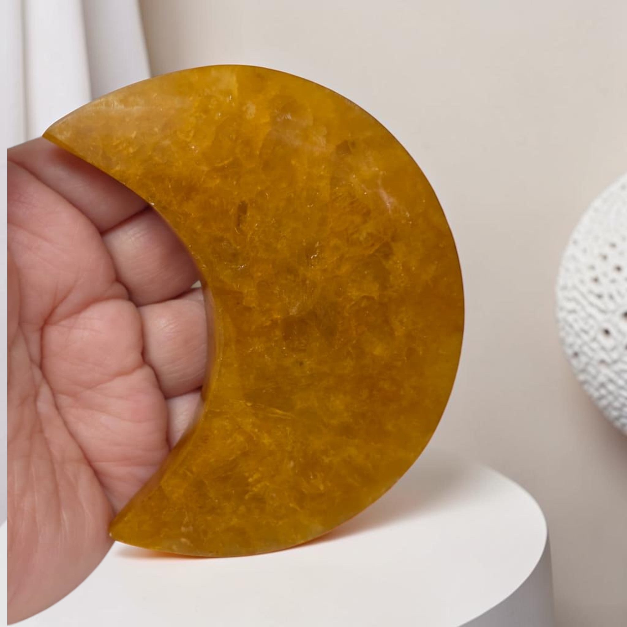 Hand holding a semi-circular amber-colored stone against a neutral background