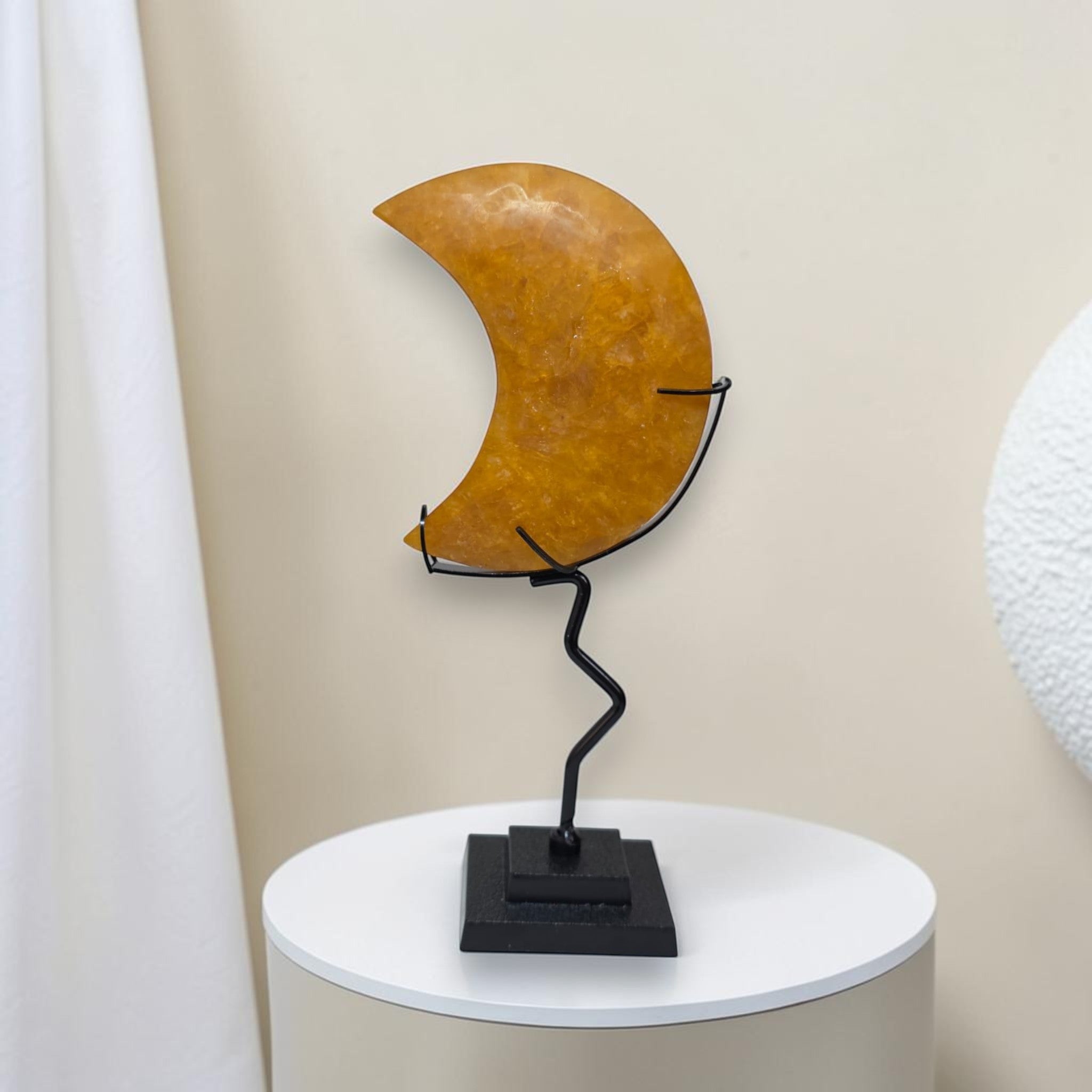 Decorative wall art with a brown crescent moon shape on a white pedestal against a beige wall.