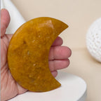 Hand holding a yellowish semi-circular stone against a beige background