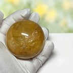 Golden Healer Quartz sphere held in gloved hand showing size and color