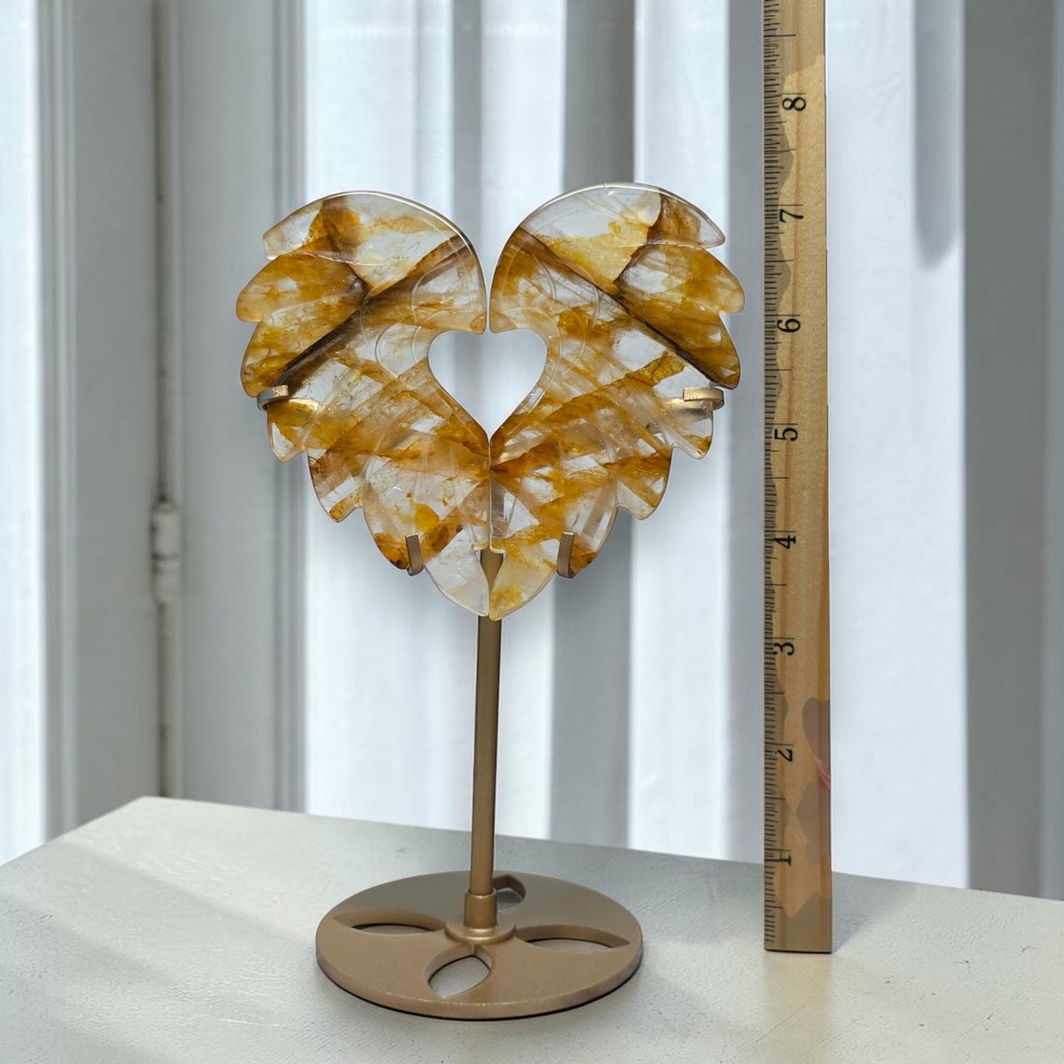 Golden Healer quartz angel wing heart with stand beside a height ruler