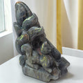 A carved stone figurine of a fox and cat on a base, displayed on a white surface with a window and curtains in the background.