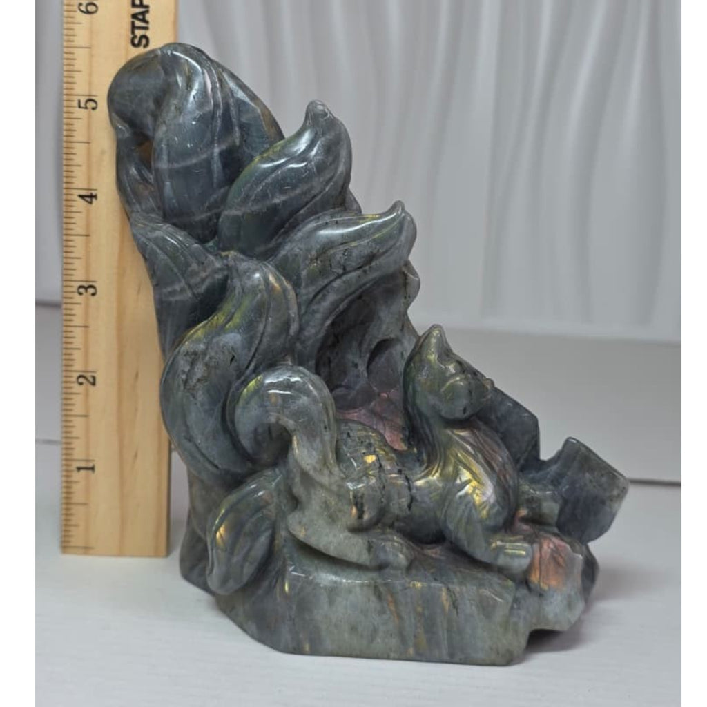 A carved stone figurine of a fox or rabbit among stylized leaves, shown next to a wooden ruler for scale against a light gray draped background.