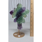 Rainbow fluorite cross sculpture with carved rose details beside measuring tape on stand