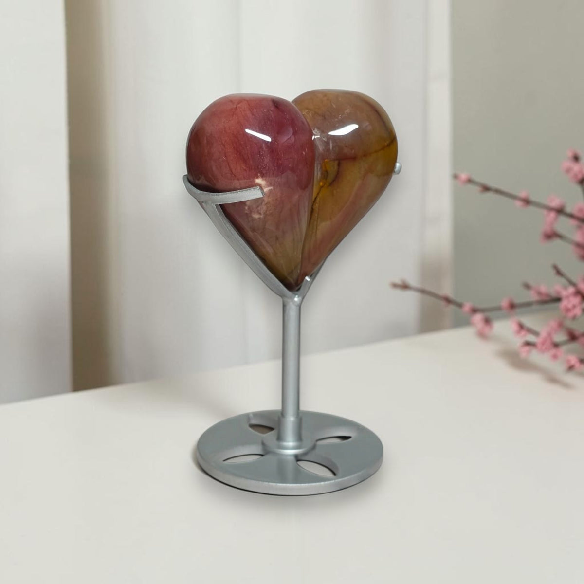 A heart-shaped glass candle holder with a silver metal stand, featuring a glossy heart design with red and amber-brown tones, displayed on a white surface.