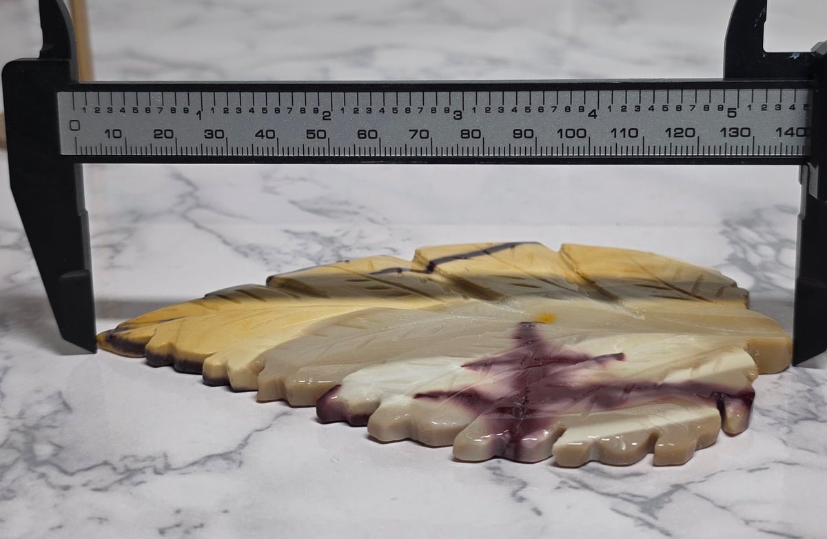 Yellow Mookaite Jasper leaf carving between caliper jaws