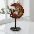 Banded agate moon fairy carving on stand, front view showing fairy silhouette in window light