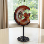 Moon crystal sculpture with fairy carving and druzy geode, on black stand, angled view