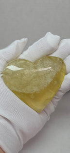 Heart-shaped crystal held by a gloved hand on a neutral background