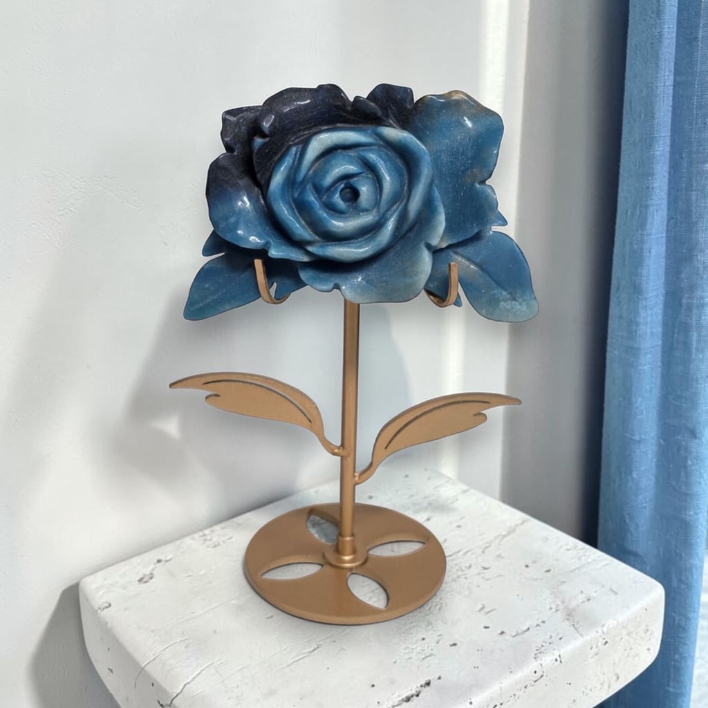 Natural Trolleite rose carving on gold stand displayed by window with blue curtains, front view