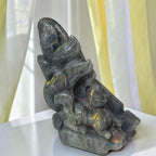 A carved stone figurine of a fox and a small animal, possibly a cat or mouse, set against a background of sheer white curtains with yellow lighting.
