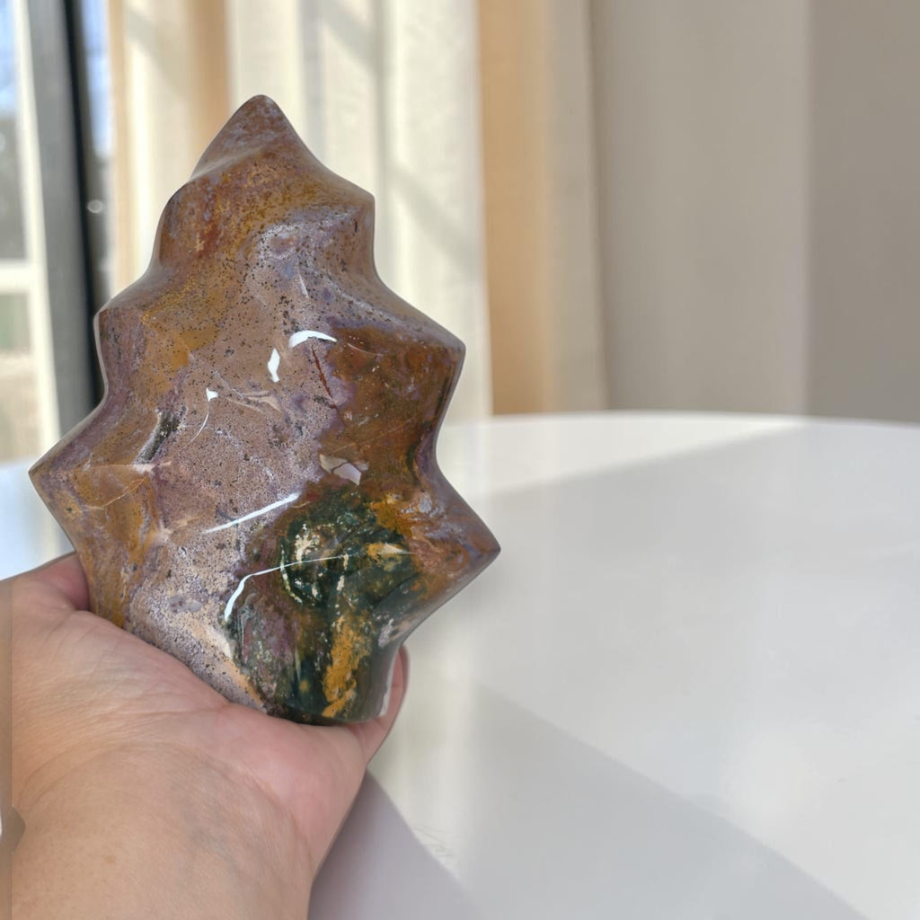 Flame-shaped ocean jasper stone in hand, brown and purple with green flecks