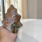 Flame-shaped ocean jasper stone in hand, brown and purple with green flecks