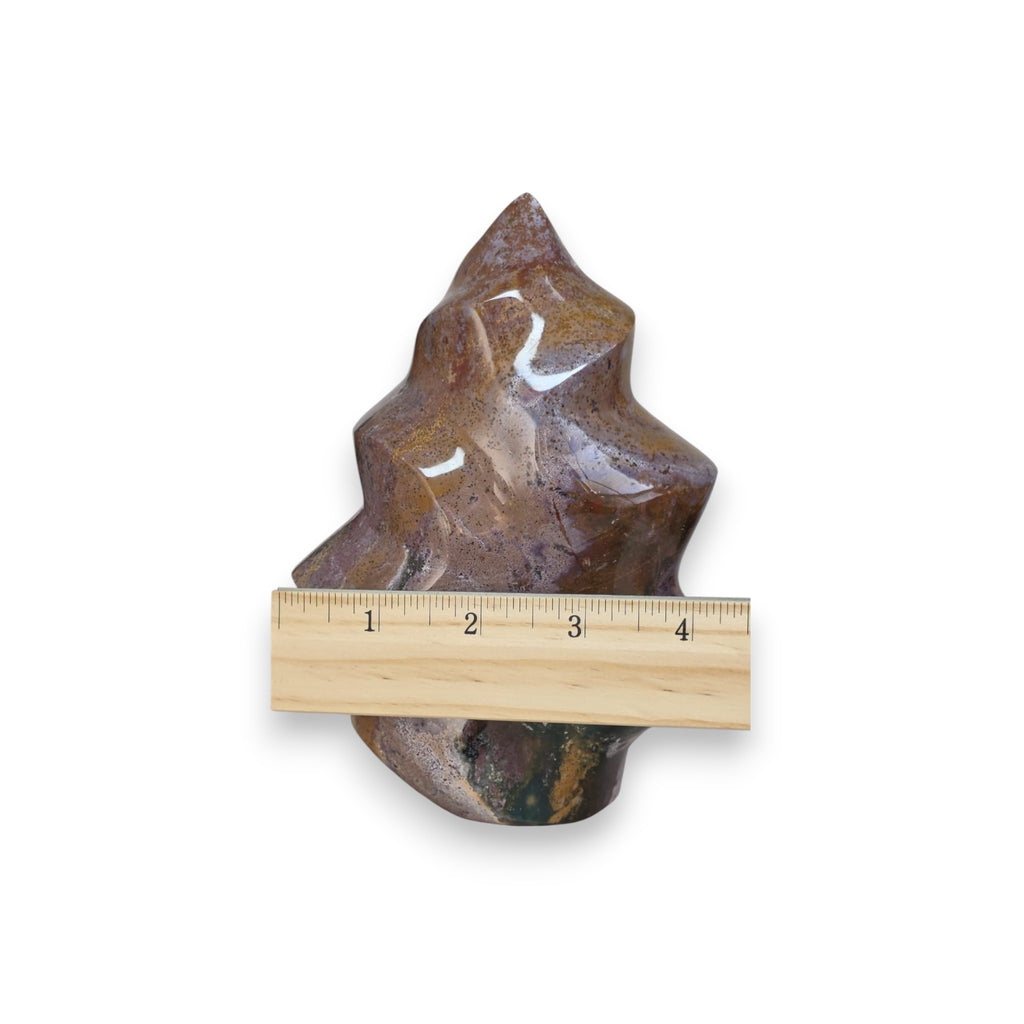 Flame-shaped ocean jasper stone with wooden ruler; brown, purple, and green veining